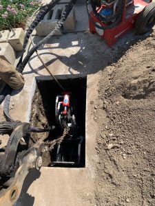 Pipe bursting 'tugger' being lowered into dug hole for new sewer line repair.